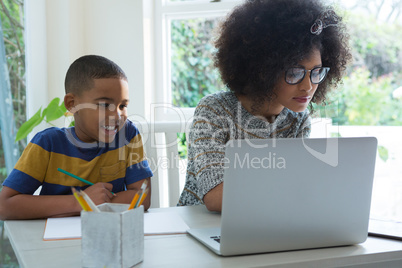 Son dosing homework while mother using laptop