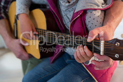 Father assisting his daughter in playing guitar