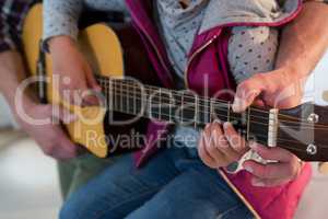 Father assisting his daughter in playing guitar