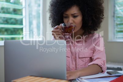 Woman having lemon tea while using laptop at desk