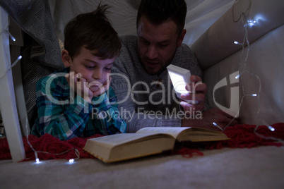Father and son reading book under shelter