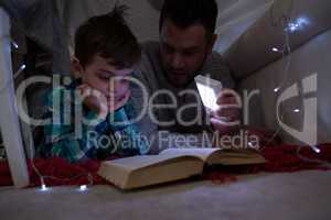 Father and son reading book under shelter