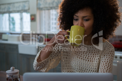 Beautiful woman having coffee while using laptop