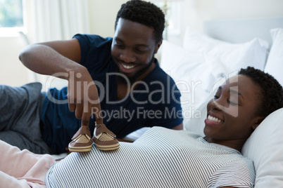 Man placing baby shoes on womans belly in bedroom