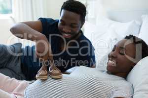 Man placing baby shoes on womans belly in bedroom