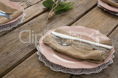 Plates with napkin, fork and butter knife arranged on wooden table