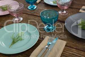 Plates with napkin, fork, butter knife and flower arranged on wooden table