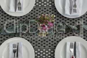 Plates with napkin, fork, butter knife and flower arranged on wooden table