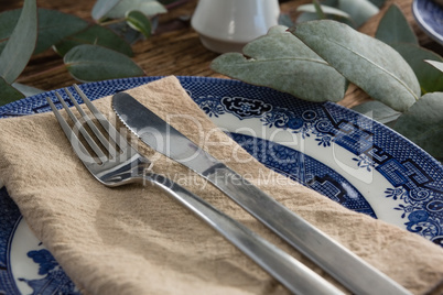 Plate with fork, butter knife and napkin on wooden table