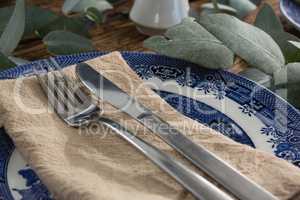 Plate with fork, butter knife and napkin on wooden table