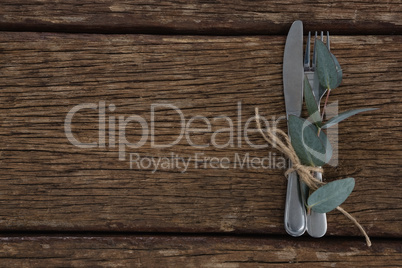 Fork, butter knife tied up with leaf on wooden table