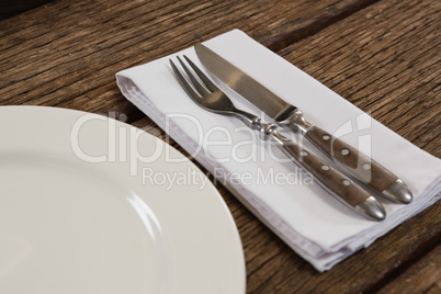 Plate with cutlery and napkin on wooden table