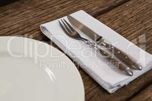 Plate with cutlery and napkin on wooden table