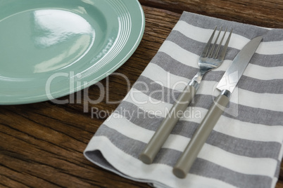 Plate with cutlery and napkin on wooden table