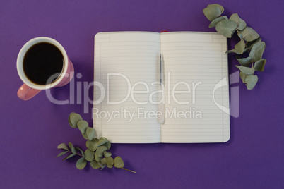 Dry leaves, black coffee, pen and book on purple background