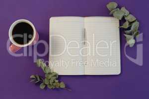 Dry leaves, black coffee, pen and book on purple background