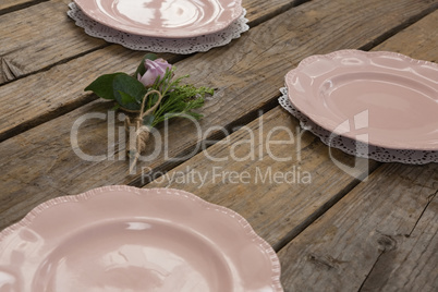 Plates with rose flower arranged on wooden table