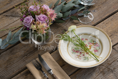 Fork and butter knife with plate and flower arranged on wooden table