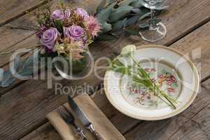 Fork and butter knife with plate and flower arranged on wooden table