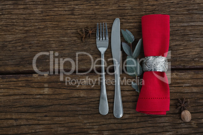 Fork and butter knife with ingredients, leaf and napkin on wooden table