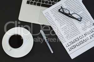 Cup of coffee, laptop, spectacles, newspaper and pen on black background