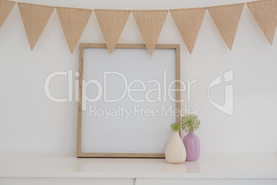Vase, bunting and blank picture frame against white wall