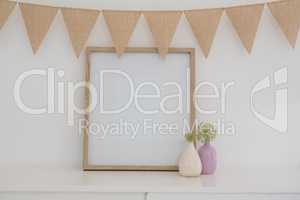 Vase, bunting and blank picture frame against white wall