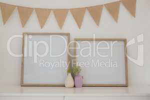 Vase, bunting and blank picture frame against white wall