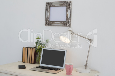 Electronic gadgets, lamp, book, mug, flora and book on table