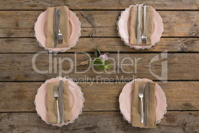 Plates with napkin, fork, butter knife and rose flower arranged on wooden table