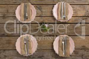 Plates with napkin, fork, butter knife and rose flower arranged on wooden table