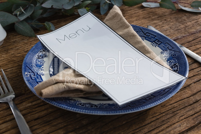 Plate with fork, butter knife, napkin and menu card on wooden table
