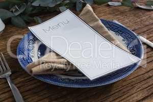 Plate with fork, butter knife, napkin and menu card on wooden table