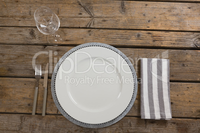 Plate, wine glass, napkin with fork and butter knife on wooden table