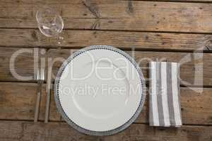 Plate, wine glass, napkin with fork and butter knife on wooden table