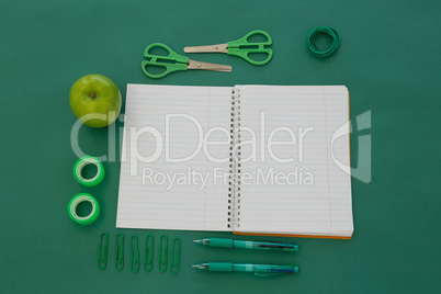 Office supplies and apple on green background