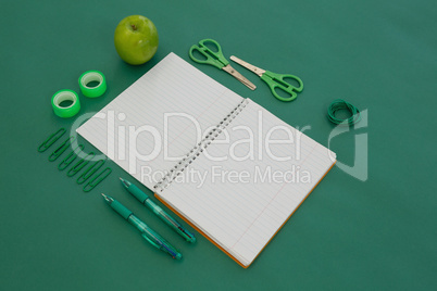 Office supplies and apple on green background