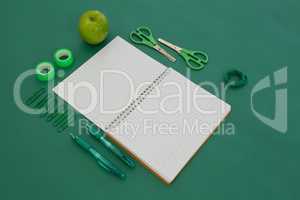 Office supplies and apple on green background