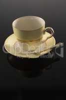 Empty cup with saucer and spoon on black background