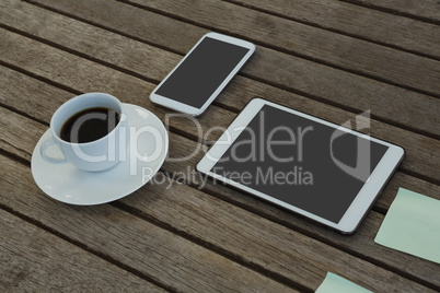 Electronic gadgets, black coffee and sticky note on wooden plank