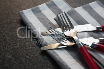 Various cutlery and folded napkin on concrete background