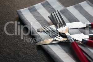 Various cutlery and folded napkin on concrete background