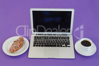 Laptop, croissant and black coffee on purple background
