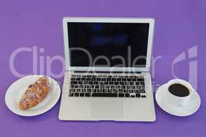 Laptop, croissant and black coffee on purple background