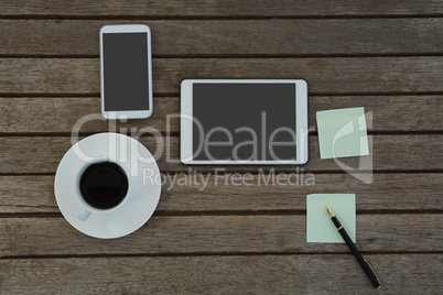 Electronic gadgets, black coffee, pen and sticky note on wooden plank