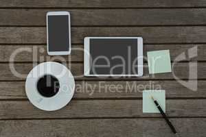 Electronic gadgets, black coffee, pen and sticky note on wooden plank