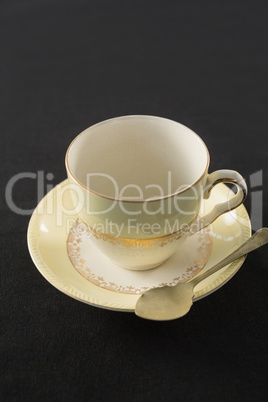 Empty cup with saucer and spoon on black background
