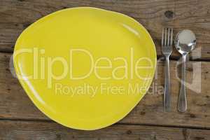 Yellow plate with fork and spoon on wooden table