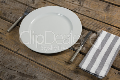 Plate with cutlery and napkin on wooden table