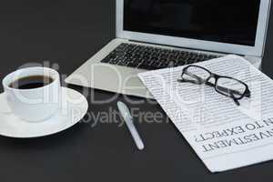 Cup of coffee, laptop, spectacles, newspaper and pen on black background